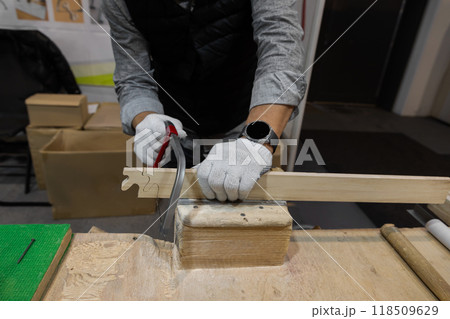 male hands in work gloves sawing wooden blank with thin hand saw male hands in work gloves sawing wooden blank with thin hand saw 118509629