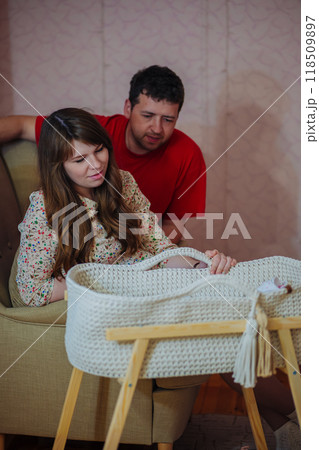 Young couple is watching over their baby who is sleeping in a moses basket at home. 118509897