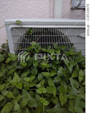 草に覆われたエアコンの室外機のアップ 118510070