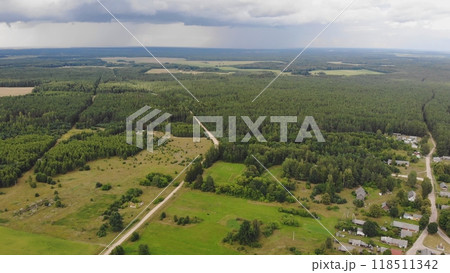 Aerial drone view of expansive woodland and a winding road leading to a quaint village on a cloudy summer day 118511342