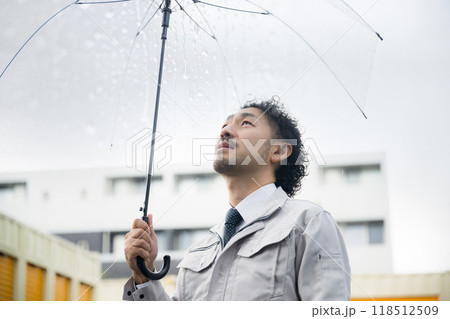 現場で雨が降る傘をさす作業着の男性 工期が遅れるので困る 現場で雨が降る傘をさす作業着の男性 工期が遅れるので困る 118512509