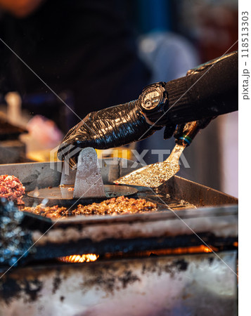 Hand in Black Glove Grilling Meat on a Hot Plate 118513303