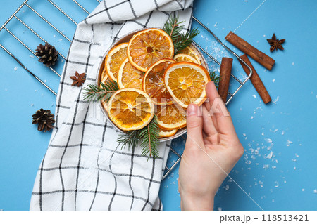 Dried orange slices in bowl, towel, hand and grid on blue background, top view 118513421