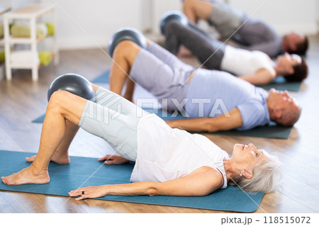 Group of mature women and men practicing pilates with soft ball in fitness studio 118515072