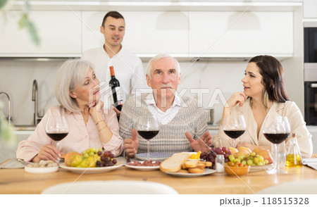 Senior parents and young couple sitting at table drinking wine and having conversation Senior parents and young couple sitting at table drinking wine and having conversation 118515328