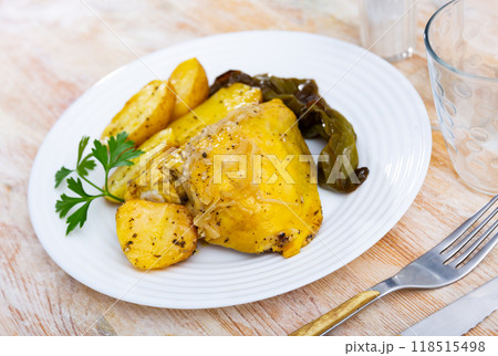 Appetizing fried chicken thigh with sliced potatoes, baked bell pepper and onions decorated with fresh of greenery on plate 118515498