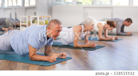 Pensioners in sportswear performing plank exercise during group Pilates workout in fitness studio 118515532