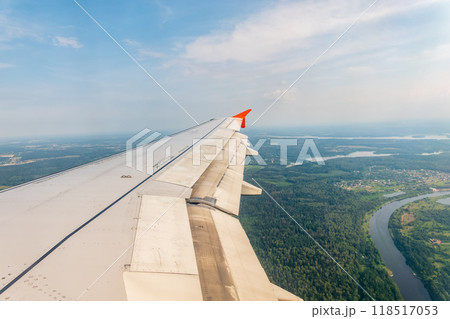 View of airplane wing, blue skies and green land during landing. Airplane window view. View of airplane wing, blue skies and green land during landing. Airplane window view. 118517053