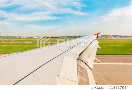 View of airplane wing, blue skies and green land during landing. Airplane window view. View of airplane wing, blue skies and green land during landing. Airplane window view. 118517054