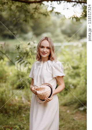 Woman standing in park holding straw hat.  118517324