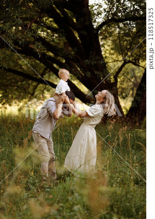 A happy family in the park in the summer. The father cheerfully lifts the child up above himself. 118517325