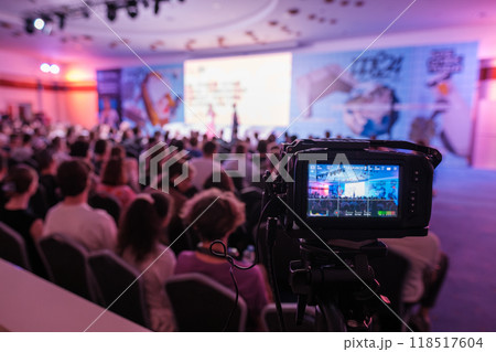 Professional video camera recording conference with audience in background 118517604