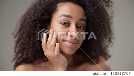 Beauty and healthcare concept - beautiful African American woman with curly afro hairstyle and clean, healthy skin touches her cheek and face with her hand, posing and looking at the camera Beauty and healthcare concept - beautiful African American woman with curly afro hairstyle and clean, healthy skin touches her cheek and face with her hand, posing and looking at the camera 118518767