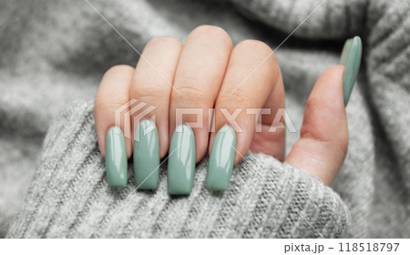 Elegant hand with long, mint-green nails resting on a cozy gray sweater 118518797