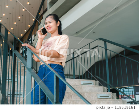 An attractive, Asian woman in fashionable is talking on the phone while standing in front of the building or shopping mall. People and wireless technology concepts, City life, Wireless technology. 118519161