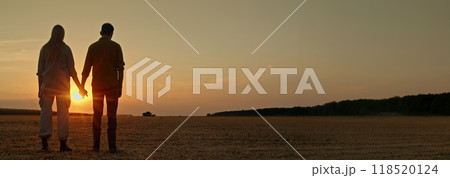 A young farming couple holds hands in a field at sunset, with a combine harvesting in the background. A young farming couple holds hands in a field at sunset, with a combine harvesting in the background. 118520124