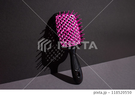 Vertical hairbrush leans against sunlit black wall, dramatic shadow below. Pink and black 118520550