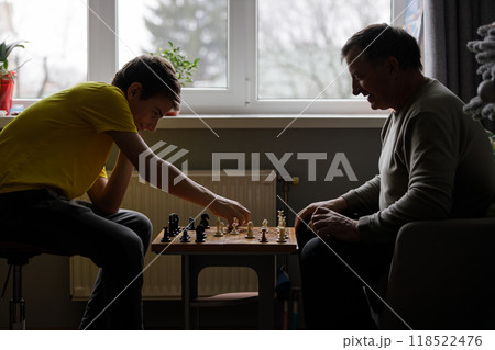 Young teenage boy and older man enjoying a chess game indoors during daylight hours 118522476