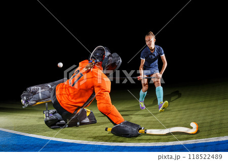Intense field hockey action between goalkeeper and forward against black background 118522489