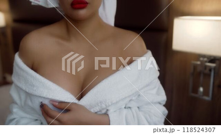 Woman gracefully adjusting her bathrobe in a luxurious hotel room setting. 118524307
