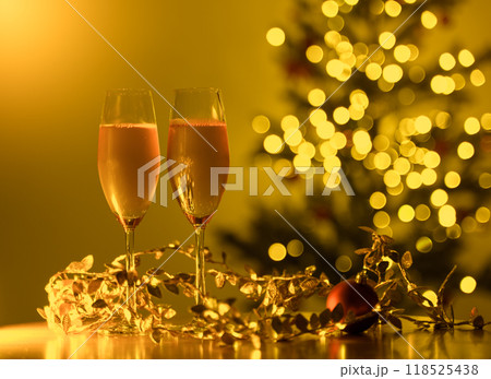 Two glasses of champagne on table in front of Christmas tree with yellow bokeh lights. Christmas and New Year celebration concept Two glasses of champagne on table in front of Christmas tree with yellow bokeh lights. Christmas and New Year celebration concept 118525438