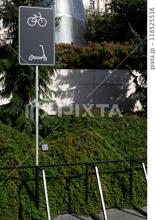 Special area with metal structure for securing bicycles and scooters in park next to sign indicating the parking area for personal mobile vehicles with locker 118525516