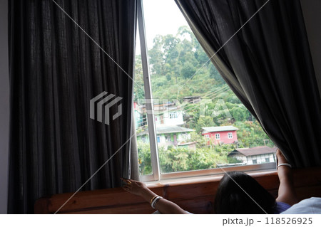 Young tourist slide curtain to take view of Moutain from window at Lingtham east Sikkim 118526925