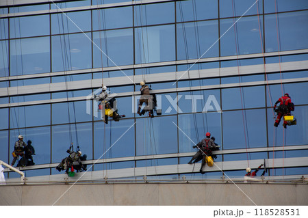 Group of climbers clean glass of skyscraper on special mounts with insurance, hard work at height, cleaning the exterior of glass office building Group of climbers clean glass of skyscraper on special mounts with insurance, hard work at height, cleaning the exterior of glass office building 118528531