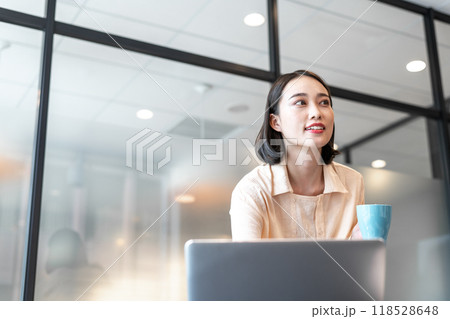 パソコン作業の合間にコーヒーを飲みながらビジネスパートナーの方へ目線を向ける女性 パソコン作業の合間にコーヒーを飲みながらビジネスパートナーの方へ目線を向ける女性 118528648
