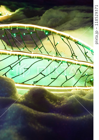 New Year LED garland in the form of a tree leaf on snow. Festive vertical template, holiday background with copy space. Neon decorative lighting in winter. New Year LED garland in the form of a tree leaf on snow. Festive vertical template, holiday background with copy space. Neon decorative lighting in winter. 118529371