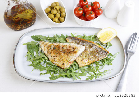 Fried dorado fillet with crispy skin. Arugula, cherry tomatoes, olives, lemon and olive oil. Traditional Mediterranean dish. White background. Selective focus, close-up. 118529583