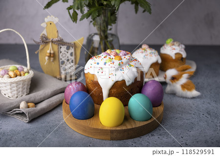 Easter kulich with candied fruits in white glaze with colorful sprinkles and painted eggs. Traditional Easter pastry. Easter holiday. Close-up, selective focus. Easter kulich with candied fruits in white glaze with colorful sprinkles and painted eggs. Traditional Easter pastry. Easter holiday. Close-up, selective focus. 118529591