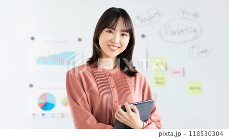 ホワイトボードの前でタブレットを持つ笑顔のビジネスウーマン 118530304