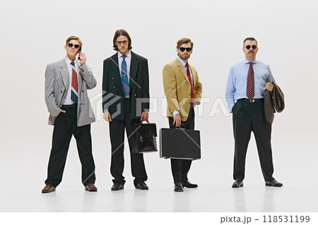 Four professionals striding confidently, carrying briefcases, exuding power and determination in oversized suits against white studio background. Four professionals striding confidently, carrying briefcases, exuding power and determination in oversized suits against white studio background. 118531199