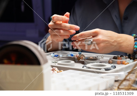 Hands of a young Caucasian woman collecting jewelry bracelets made at home. Individual jewelry made of stones and precious metals. Raw materials for making jewelry. Collection of precious stones. 118531309