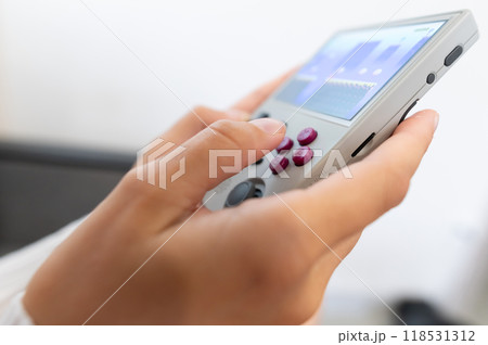 Close-up of female hands of young Caucasian woman holding retro video game console. Girl playing retro games on portable game console. Shallow depth of field. Selective focus 118531312