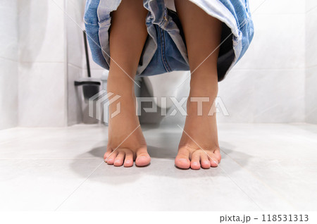 Low angle. A woman sits on the toilet bowl in the bathroom, and she takes off her pants shorts in the bathroom. She had a stomach ache and was dissatisfied with constipation, diarrhea, food poisoning 118531313