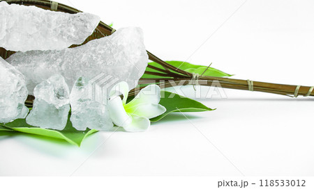 Clear and pristine alum cubes resting in a bamboo basket alongside leaves, set against a white background. 118533012