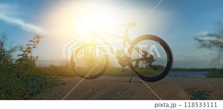 Black bicycle parked on the sand dunes Behind them, the sun shines at dusk. Black bicycle parked on the sand dunes Behind them, the sun shines at dusk. 118533111