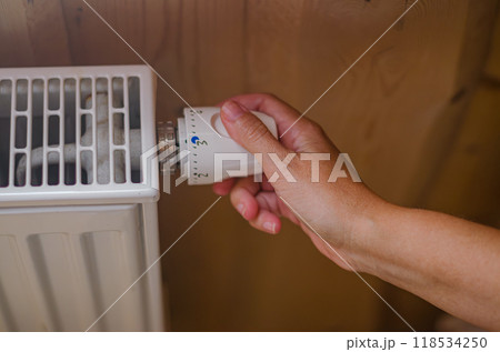 Closeup on woman's hand adjusting thermostat valve in wooden house. High quality photo Closeup on woman's hand adjusting thermostat valve in wooden house. High quality photo 118534250