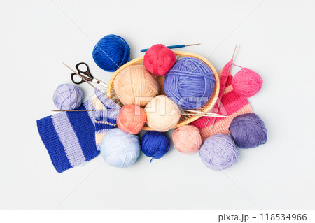 Blue, pink and beige knitting balls in basket with knitting needles and knitted scarf on gray background. Set for the hobby of knitting warm clothes or toys. Concept needlework 118534966
