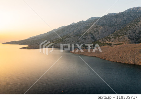 Coastal village among rugged mountains surrounded by sea . Small houses with red-tiled roofs and lush greenery create picturesque scene 118535717