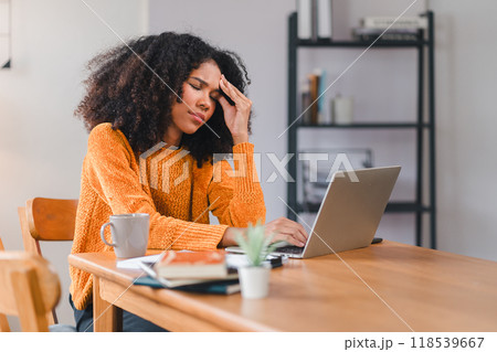 African American woman holding her forehead in frustration while working on a laptop, showcasing stress and exhaustion. 118539667