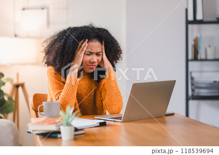 African American woman holding her forehead in frustration while working on a laptop, showcasing stress and exhaustion. African American woman holding her forehead in frustration while working on a laptop, showcasing stress and exhaustion. 118539694