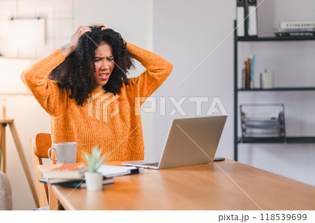 African American woman holding her forehead in frustration while working on a laptop, showcasing stress and exhaustion. African American woman holding her forehead in frustration while working on a laptop, showcasing stress and exhaustion. 118539699