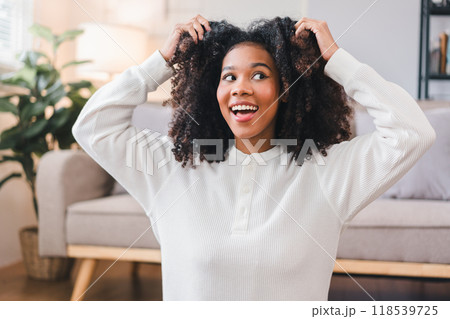 Excited African American Woman Playing with Curly Hair at Home. 118539725