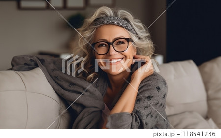 In her sunlit living room, the modern elderly woman exudes sophistication, wearing glasses, creating a chic and cozy atmosphere. 118541236