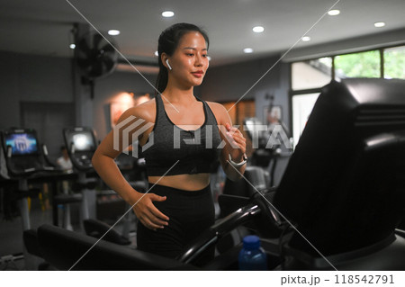 Young athletic woman running on treadmill in modern fitness gym. Healthy lifestyle Young athletic woman running on treadmill in modern fitness gym. Healthy lifestyle 118542791