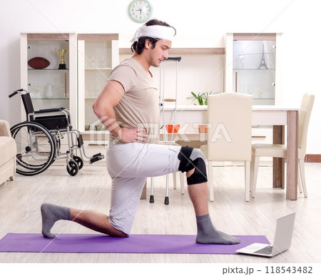 Injured young man doing exercises at home 118543482