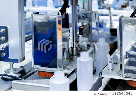 robot arm moving plastic bottle to conveyor belt of auto capping and labeling machine at cosmetic and skin care manufacturing. cosmetic industry and ai technology machinery concept. robot arm moving plastic bottle to conveyor belt of auto capping and labeling machine at cosmetic and skin care manufacturing. cosmetic industry and ai technology machinery concept. 118545049